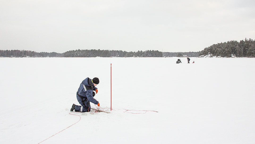 Kalastaja kokemassa verkkojaan meren jäällä talvella.